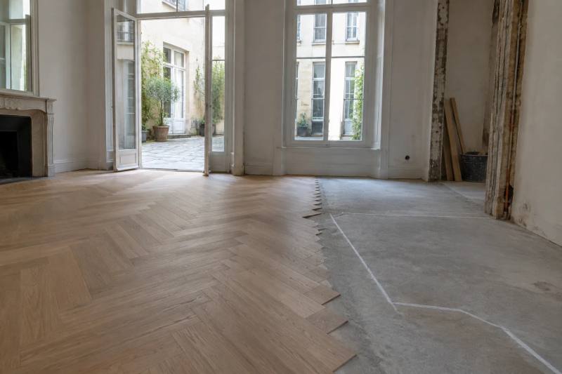 New herringbone oak parquet meeting bare screed on a Paris flat floor, with a chalk layout line